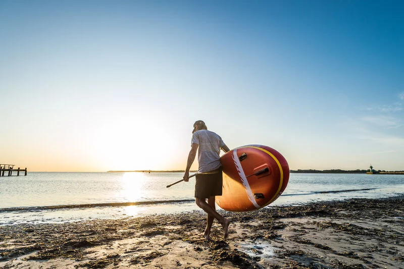 Ein Mann läuft mit einem Stand-Up-Paddle ins Wasser am Strand